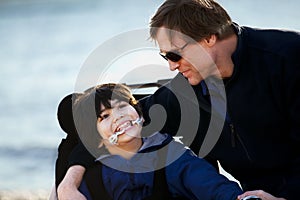 Father sitting with disabled son along lake shore