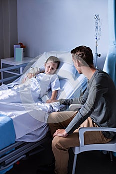 Father sitting beside her daughter lying on a hospital bed