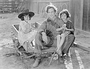 Father sitting with his two daughters on a small wagon on a farm