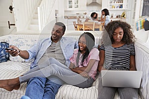 Father Sitting On Sofa Watching TV With Teenage Daughters