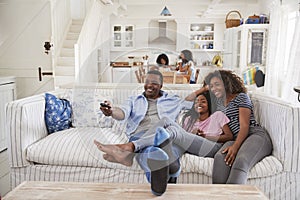 Father Sitting On Sofa Watching TV With Teenage Daughters