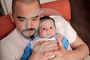 Father sleeping in armchair while holding infant daughter. Baby is awake. Lack of sleep for young parents concept