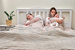 Father sleeps while mother takes care of baby boy, parents and infant child on home bed. Problems of a man and a woman with a