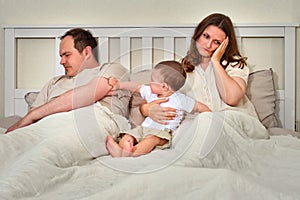 Father sleeps while mother takes care of baby boy, parents and infant c
