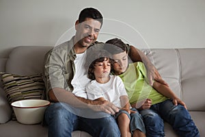 Father and sleepy sons with popcorn bowl watching tv in living room
