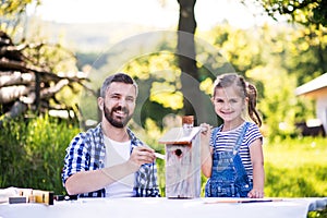 Father with a small daughter outside, painting wooden birdhouse.