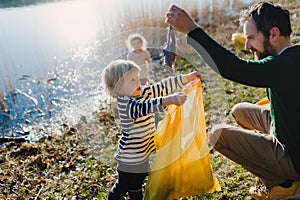 Father with small kids collecting rubbish outdoors in nature, plogging concept.