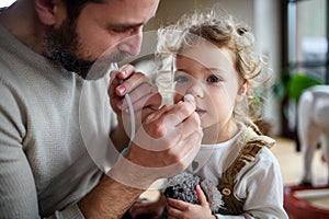 Father with small sick daughter indoors at home, using nasal aspirator. photo