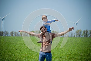 Father with a small son on his shoulders fly near the blades of the wind generator