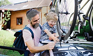 Father with small son putting bicycles on car roof, going on trip concept.