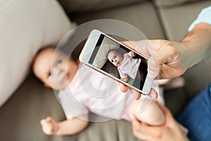 Father with smartphone taking picture baby at home