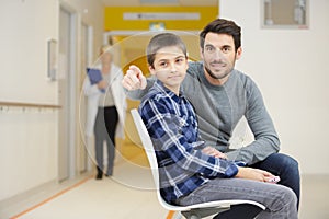 father with smiling son while waiting for doctor in hospital