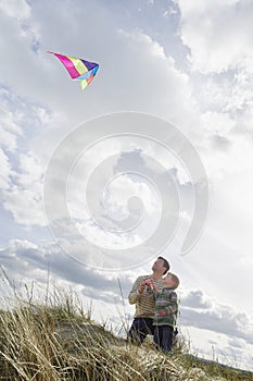 Father and son (5-6) flying kite on dunes