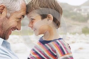 Father and son (5-6) touching foreheads on beach close-up