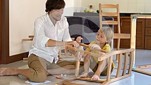 Father and son assemble wooden furniture from small parts. Little boy helps his father to assemble a chair.