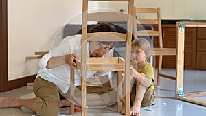 Father and son assemble wooden furniture from small parts. Little boy helps his father to assemble a chair.