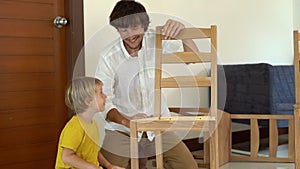 Father and son assemble wooden furniture from small parts. Little boy helps his father to assemble a chair.