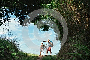 Father and son backpackers hiking by the forest pathway, taking a short rest break. Happy parents travelling with kids concept