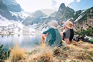 Father and son backpackers sit near the mountain lake and enjoy