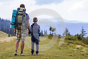 Father and son with backpacks hiking together in scenic summer green mountains. Dad and child standing enjoying landscape mountain