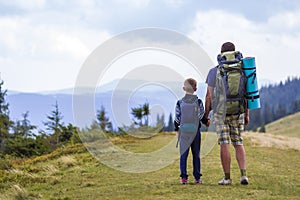 Father and son with backpacks hiking together in scenic summer green mountains. Dad and child standing enjoying landscape mountain