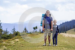 Father and son with backpacks hiking together in scenic summer green mountains. Dad and child standing enjoying landscape mountain