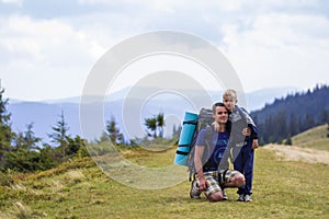 Father and son with backpacks hiking together in scenic summer green mountains. Dad and child standing enjoying landscape mountain