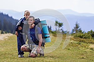 Father and son with backpacks hiking together in scenic summer green mountains. Dad and child standing enjoying landscape mountain