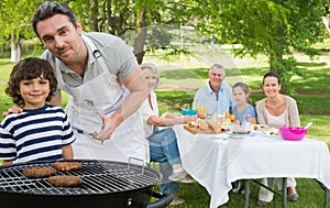 Father and son at barbecue grill with family having lunch in park