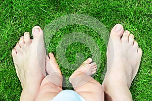 Father and son bare feet on green grass lawn at park. Parent with baby boy making first steps in life.Child exploring