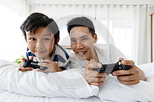 The father and son in bed of the Asian family have fun and happy playing video games on the bed in the room. Concept in a holiday