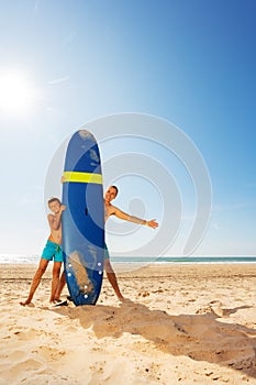 Father and son behind surf board on the sand beach