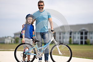 Father and son in bike helmet learning ride bicycle. Father and son on bicycle on summer day outdoor. Little son trying