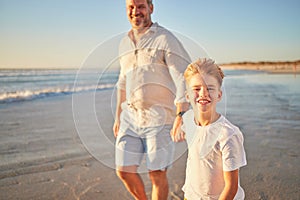 Father and son bonding on a beach, walking alone the ocean and holding hands at sunset. Portrait of an excited child