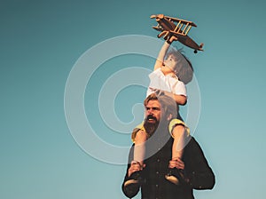 Father and son. Boy with toy aeroplane sitting on fathers shoulders. Happy father child moment. Father piggybacking his