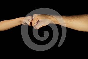 Father and son bump their fists. Isolated men and children hands on a black background.