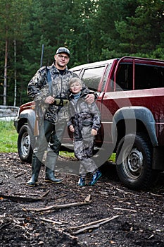 Father and son came to the forest for hunting together. Standing with a shotgun rifle in front of pickup truck.