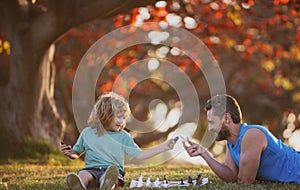 Father and son child playing chess spending time together in park.