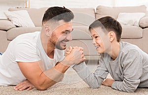 Father and son compete in arm-wrestling, lying on floor at home