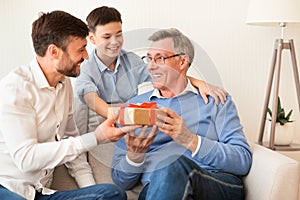 Father And Son Congratulating Grandpa Giving Birthday Gift At Home