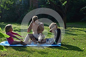 Father, son and daughter are doing gymnastics in the garden