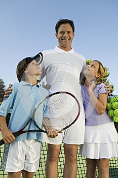 Father with Son and Daughter by net on Tennis Court portrait front view