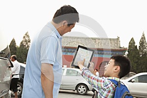 Father and son with digital tablet, son smiling and pointing, outdoors