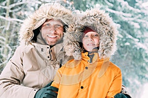 Father and son dressed in Warm Hooded Casual Parka Jacket Outerwear walking in snowy forest cheerful smiling faces portrait.