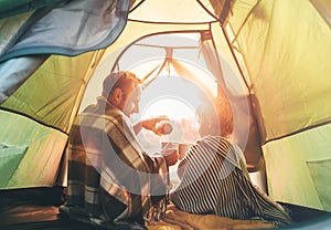 Father and son drink hot tea sitting together in camping tent