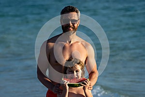 Father and son eat juicy red watermelon on beach. Summer kid holidays, seasonal fruits and berries. Summer father and