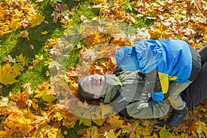 Father and son family playful fighting aerial portrait at yellow and orange autumn fallen leaves groundcover