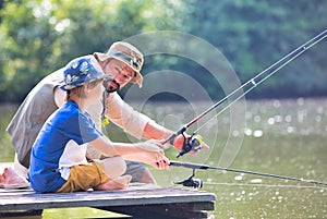 Father and son fishing in Lake while sitting on pier