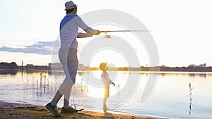 Father and son fishing on the shore of the river at sunset