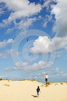 Father and Son Flying Kite on sand dune on beach